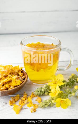 Kräutertee-Getränk aus Verbascum thapsus, der großen Königskerze, der Großen Königskerze oder der gemeinen Königskerze. Gelbe getrocknete Blütenblätter. Glasbecher. Stockfoto