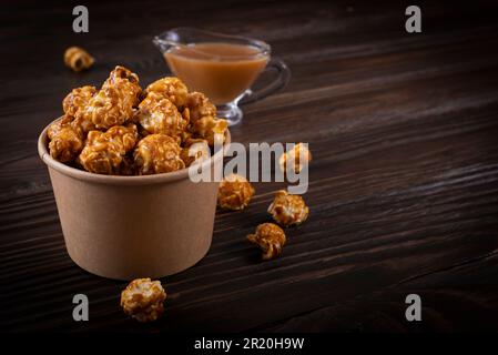 Karamellisiertes Popcorn in Papiereimer auf Holztisch Stockfoto