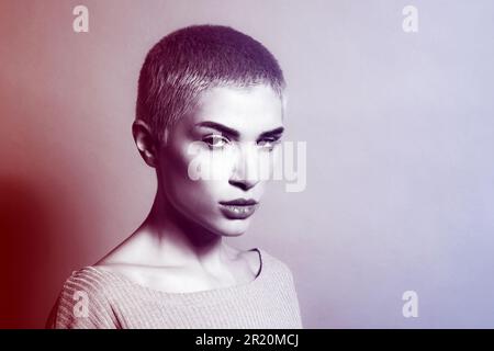 Porträt einer jungen, ernsten Frau mit kurzen Haaren, die vor dem Studiohintergrund in die Kamera schaut Stockfoto