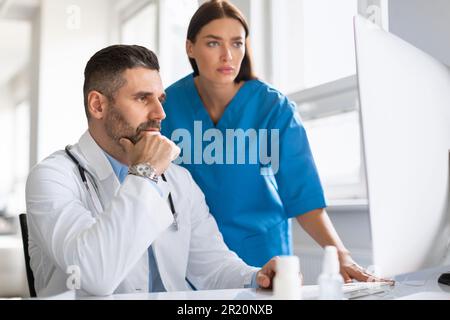 Diagnosediskussion. Fokussierter männlicher Arzt und seine Assistentin bei der Analyse medizinischer Zustände mittels Computer in der Klinik Stockfoto