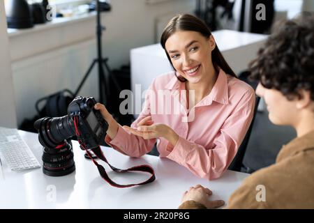 Momente festhalten. Eine junge Fotografin, die Fotos zeigt, arbeitet für ein männliches Model im Studio, spricht nach dem Fotoshooting Stockfoto