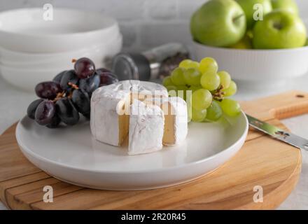 Brie oder Weichkäse mit dunklen und grünen Trauben auf einem Teller Stockfoto