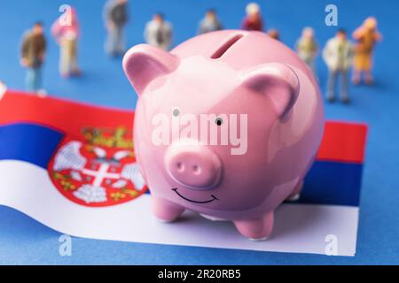Sparschwein, serbische Flagge und Spielzeugmänner aus Plastik auf farbigem Hintergrund, ein Konzept zum Thema Einkommen der serbischen Bevölkerung Stockfoto