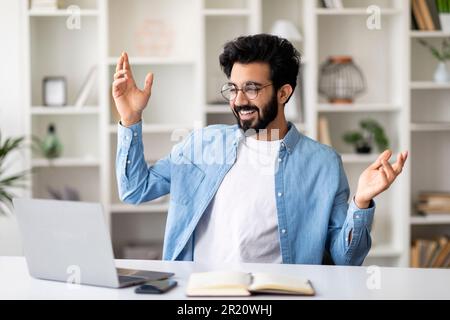 Begeisterter inder feiert geschäftlichen Erfolg mit einem Notebook im Heimbüro Stockfoto