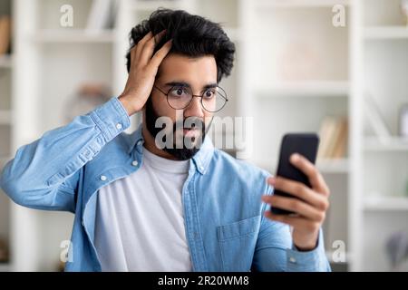 Oh Nein Schockierter Indianer, Der Auf Den Smartphone-Bildschirm Schaut Und Den Kopf Berührt Stockfoto