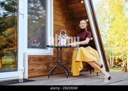 Glückliche lächelnde Frau ruht sich auf der Terrasse eines winzigen Hauses aus Stockfoto