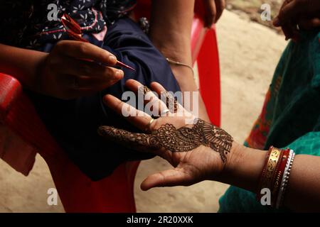 Indisches Teenager-Mädchen, das Heena Tatoo auf die Hand einer Frau aufträgt Stockfoto