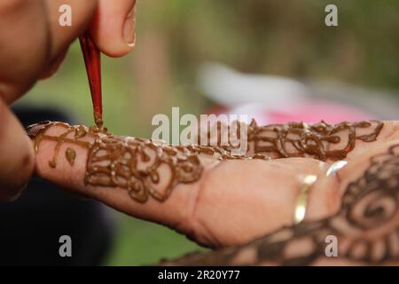 Indisches Teenager-Mädchen, das Heena Tatoo auf die Hand einer Frau aufträgt Stockfoto