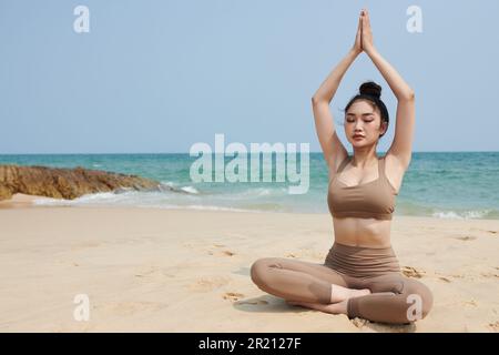 Fit, junge Frau, die Morgenmeditation am Meeresstrand genießt Stockfoto