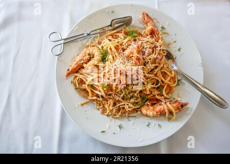 Spaghetti mit Garnelen in Tomatensauce garniert mit Kräutern und Parmesankäse auf einem Teller und einer weißen Tischdecke, Blick von oben, Kopie sp Stockfoto