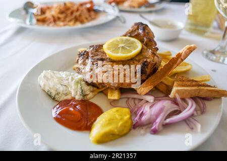 Gebratenes Schweinesteak mit Pommes Frites, Zwiebeln, verschiedenen Dips und einer Zitronenscheibe, Barbecue-Gericht im Sommer auf einem weißen Teller, ausgewählter Fokus, geringe Tiefe o Stockfoto