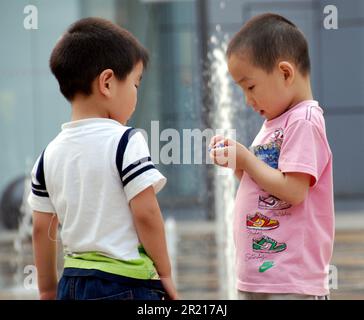 Kinder spielen an Springbrunnen im Einkaufsviertel in Sanlitun, Peking. Es gab eine "ein-Kind-Politik" , eine von 1980 bis 2015 in China durchgeführte Bevölkerungsplanungsinitiative, um das Bevölkerungswachstum des Landes zu bremsen, indem viele Familien auf ein einzelnes Kind beschränkt wurden. Diese Initiative war Teil einer viel umfassenderen Anstrengung zur Eindämmung des Bevölkerungswachstums, die 1970 begann und 2021 endete Stockfoto