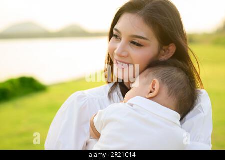 Liebevolle Mutter hält und trägt ihr Neugeborenes in einem öffentlichen Park Stockfoto