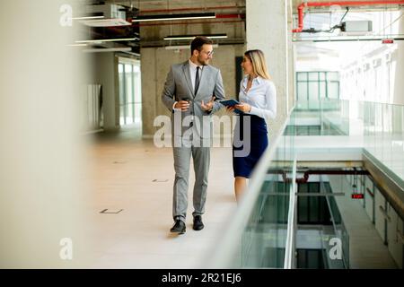 Junge Kollegen, die im modernen Büro entlang des Korridors gehen und reden Stockfoto