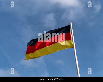 Eine deutsche Flagge auf einem Fahnenmast vor einem blauen Himmel. Stockfoto