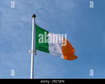 Eine irische Flagge auf einem Fahnenmast vor einem blauen Himmel. Stockfoto