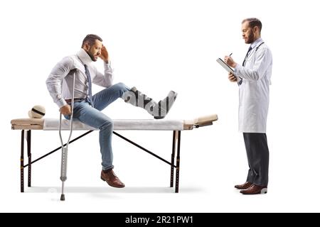 Verwundeter mit orthopädischem Stiefel und Halsband, der auf einem Therapietisch sitzt und ein Arzt ein isoliertes Dokument auf weißem Hintergrund schreibt Stockfoto