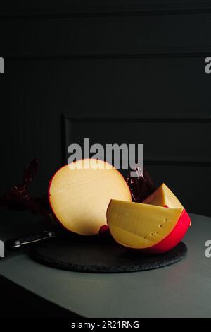 Geschnittener Kopf von Edamkäse auf dunklem Hintergrund. Stockfoto