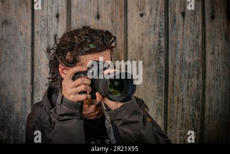 Männlich mit schwarzer Vollformatkamera und Weitwinkelobjektiv in der Nähe einer alten Holzwand Stockfoto
