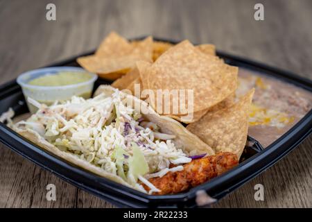 Zur Bestellung von Heilbutt-Fisch-Taco-Menü mit Bohnen und Chips, alles in einem Kunststoffbehälter mit Dressing an der Seite serviert. Stockfoto