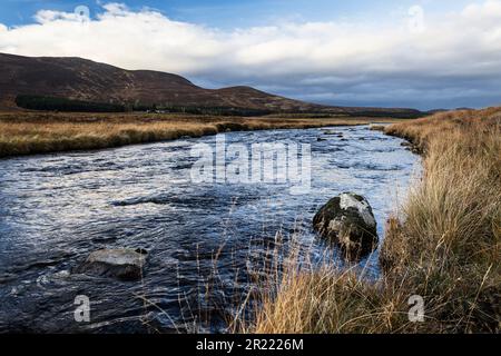 Ein Tal in den Highlands mit einem Fluss und Unterholz, einige Hügel im Hintergrund und Wolken am Himmel. Stockfoto