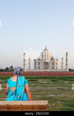 Rückansicht einer alten Frau in zyanfarbenem Sari und langen Haaren in Tress, mit Blick auf den Taj Mahal Stockfoto