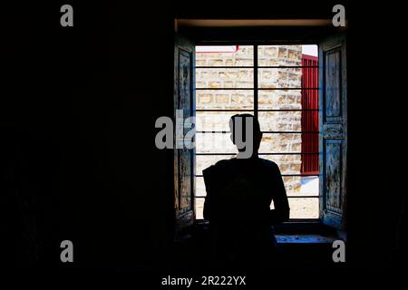 Silhouette einer Frau in einem dunklen Raum vor dem Fenster und der Sonne draußen Stockfoto