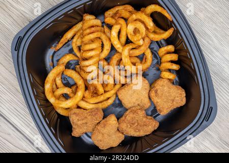 Blick von oben auf die Bestellung lockiger pommes frites und Chicken Nuggets sind in einem Kunststoffbehälter mit Dressing an der Seite verpackt. Stockfoto