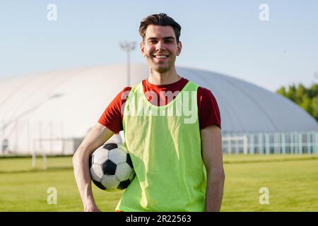Porträt eines lächelnden jungen Fußballspielers mit einem Fußball bei Sonnenuntergang Stockfoto