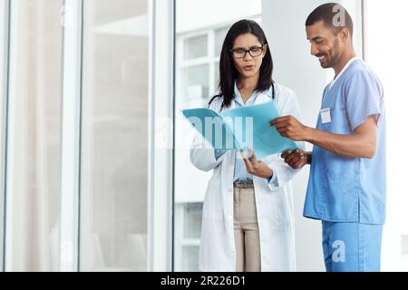 Ich wollte dir etwas sagen. Zwei junge Ärzte diskutieren den Inhalt einer Akte in einem modernen Krankenhaus. Stockfoto
