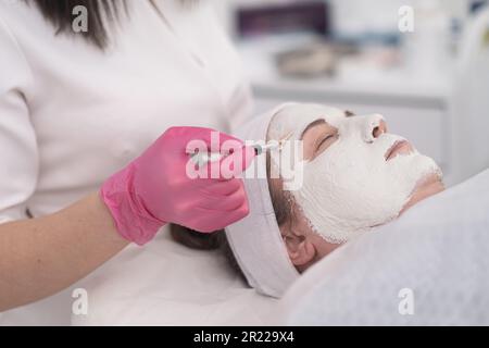 Hautpflegeexperte trägt eine pflegende Gesichtsmaske mit Pinsel für spezifische Hautprobleme auf ihren Klienten auf Stockfoto