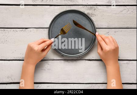 Frau, die Gabel und Messer in der Nähe einer sauberen Platte auf einem weißen Holztisch hält Stockfoto