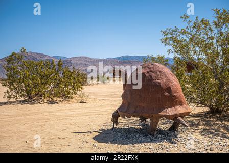 Borrego Springs, CA, USA - 24. April 2023: Prähistorische Riesenschildkrötenstatue aus braunem rostfreiem Metall auf sandigem Wüstenboden mit grünen Büschen unter blauen s Stockfoto