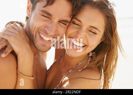 Das perfekte Bild der jungen Liebe. Ein wunderschönes junges Paar, das am Strand zusammen umarmt und lacht. Stockfoto