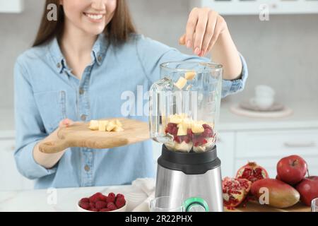 Frau gibt Mango in den Mixer mit Zutaten für Smoothie in der Küche, Nahaufnahme Stockfoto