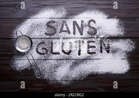 Sieb und Satz glutenfrei geschrieben auf Französisch mit Mehl auf dunklem Holztisch, flach liegend Stockfoto