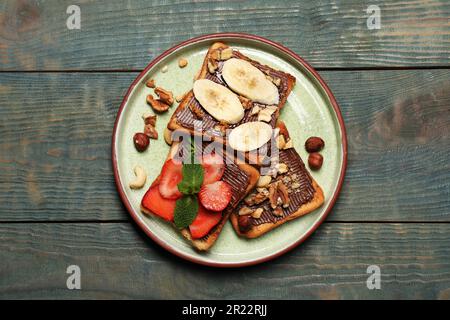 Leckere Toasts mit Schokoladenaufstrich, Nüssen, Erdbeeren, Banane und Minze, serviert auf einem Holztisch, Blick von oben Stockfoto