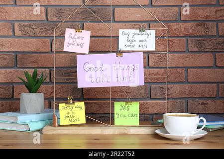 Notizen mit motivierenden Zitaten, Kaffee, Zimmerpflanzen und Büchern auf dem Tisch an einer Backsteinwand Stockfoto