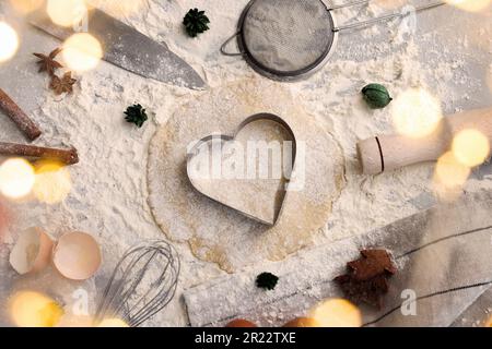 Flach liegend mit herzförmigem Keksschneider, Teig und Zutaten auf dem Tisch Stockfoto