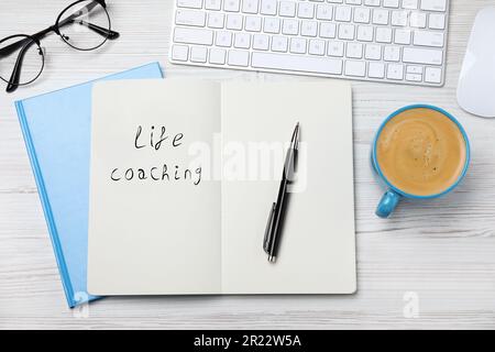 Die Phrase Life Coaching steht in Notizbuch, Stift, Tasse Kaffee, Gläsern und Tastatur auf einem weißen Holztisch, flach liegend Stockfoto