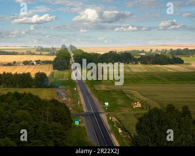 Landstraße zum Dorf zwischen Feldern vor blauem Himmel Stockfoto