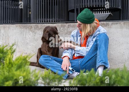 Ein unglücklicher Millennials-Typ und ein süßer, obdachloser Hund, der draußen zusammen sitzt Stockfoto