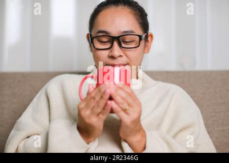 Porträt einer jungen Frau, die zu Hause eine Tasse Kaffee genießt. Eine schöne Frau im weißen Pullover, die morgens heissen Kaffee trinkt. Lifestyle, fr Stockfoto