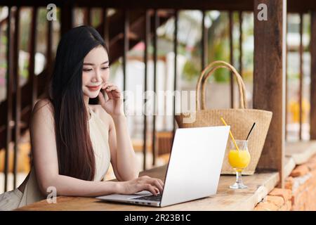 Lächelnde junge Frau, die an einem Laptop an der Strandbar arbeitet Stockfoto