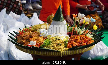 Nasi Tumpeng (Konusreis) serviert mit Urap-Uap (indonesischer Salat), gebratenem Hähnchen und Nudeln. Nasi-Tumpeng wird normalerweise auf Geburtstagspartys serviert Stockfoto