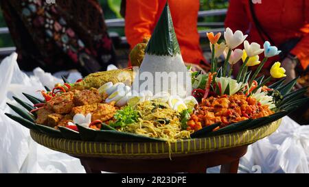 Nasi Tumpeng (Konusreis) serviert mit Urap-Uap (indonesischer Salat), gebratenem Hähnchen und Nudeln. Nasi-Tumpeng wird normalerweise auf Geburtstagspartys serviert Stockfoto