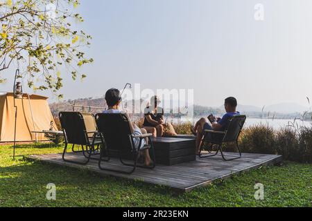 Drei beste Freunde, die im Freien campen und ihr Mobiltelefon benutzen. Stockfoto