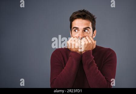 Was war das für ein Geräusch? Studiofoto eines gutaussehenden jungen Mannes, der vor grauem Hintergrund verängstigt aussieht. Stockfoto