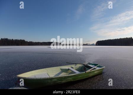 Ein Boot, das im Winter im Eis eines Waldsees festsitzt, erleuchtet durch das raue Tageslicht bei eiskalten Temperaturen. Stockfoto