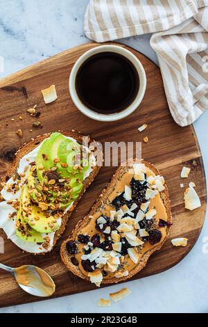 Vegane Frühstückstoasts mit Avocado und Erdnussbutter auf einem Holzbrett. Stockfoto